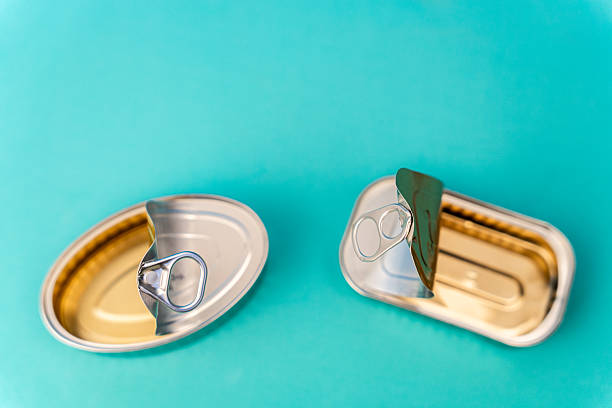 Two empty golden-colored cans with their lids open, lying on a turquoise background, creating a simple yet evocative image