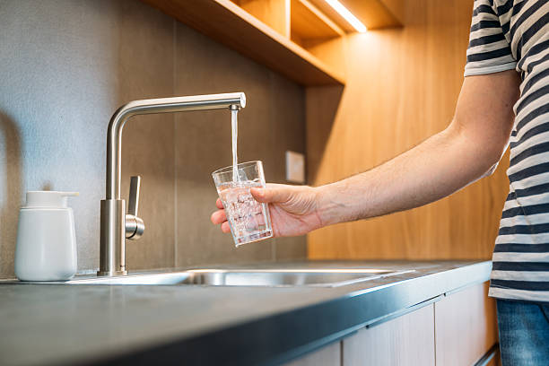 istock Man pouring tap water from kitchen faucet into drinking glass 2208950589