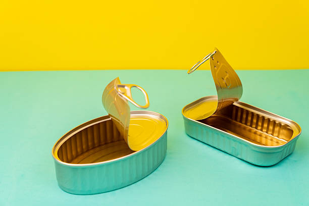 Metal tin cans lying vacant against bright yellow-turquoise surface, representing packaging waste and consumer culture remnants