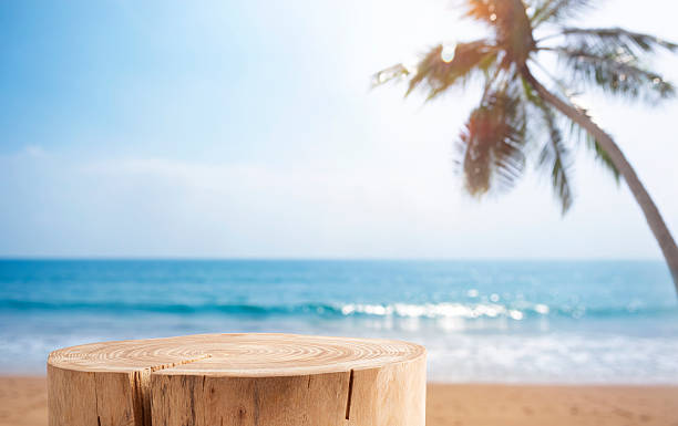 istock Stump table on sandy beach with blurred blue sea, sky and palm tree background 2208953002