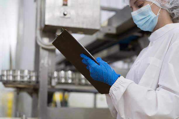istock Canned fish factory, seafood manufacturing and processing. Food processing. Conveyor belt and workers. Hands of worker inspecting quality of seafood processing conveyor belts 2208963824