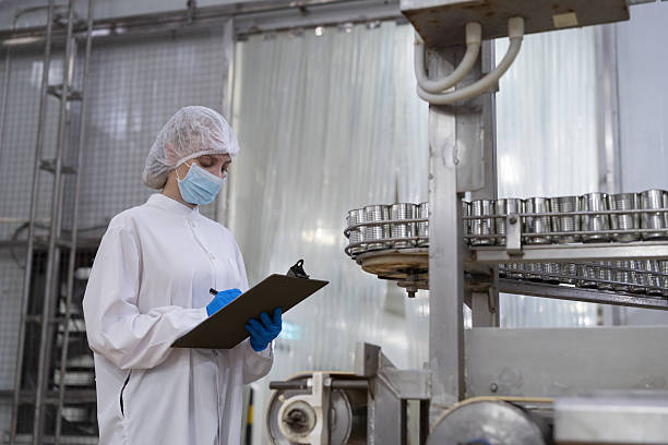 istock Canned fish factory, seafood manufacturing and processing. Food processing. Conveyor belt and workers. Worker in protective gear wearing hairnet inspecting quality of seafood processing conveyor belts 2208963826