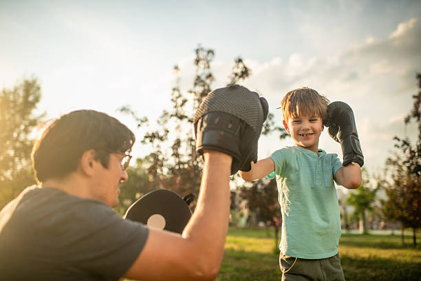 Father teaching his son boxing outdoors in a summer park Father teaching his son boxing outdoors in sunset boxing at home equipment stock pictures, royalty-free photos & images