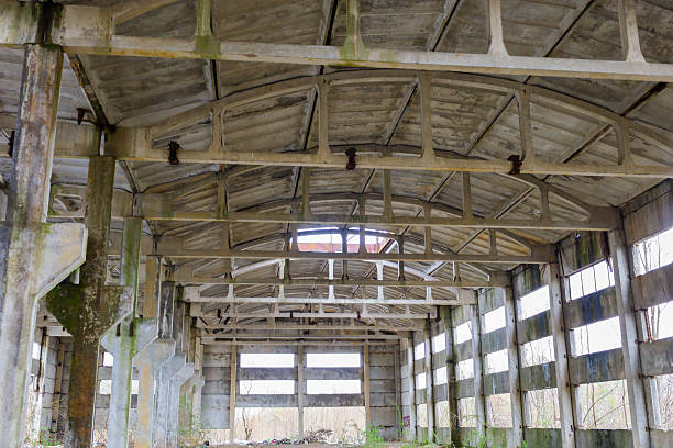 Interior of an abandoned industrial building with concrete arches and ceiling. Light penetrates through holes in the roof and broken windows, creating a play of shadows.
