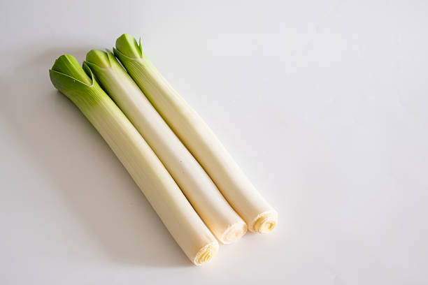 A visually balanced composition featuring fresh green onions arranged in parallel with wooden chopsticks on a white background. This minimalist food styling highlights the natural beauty of fresh ingredients, emphasizing Asian cuisine, plant-based diets, and healthy eating. The clean and modern presentation makes it ideal for culinary content, food photography, and nutrition-focused designs.