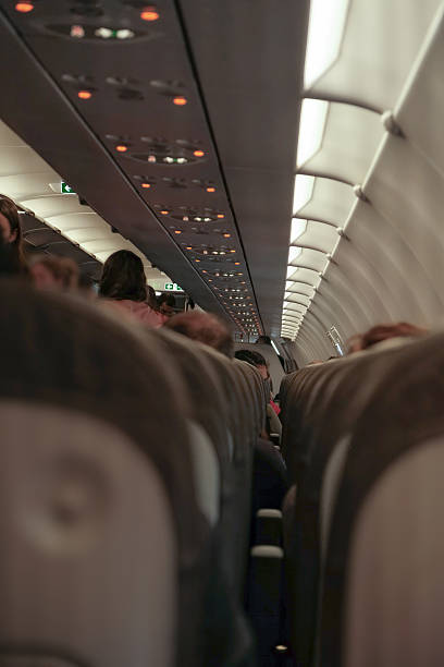 istock Interior scene of airplane, passengers boarding and looking for their seats.Low angle view, shot from back of plane with shallow depth of field. Travellers getting ready for take off 2208978885