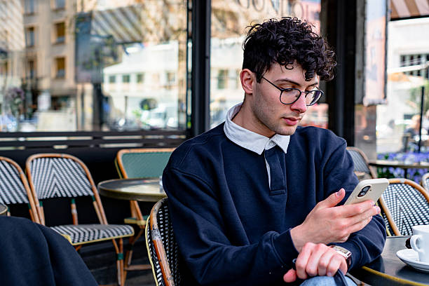 istock Young man using smartphone in Parisian outdoor cafe 2208982818