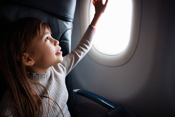 Charming kid traveling by an airplane. Little girl sitting by aircraft window during the flight. Air travel with kids