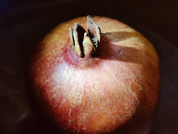 Close-up shot of a ripe pomegranate fruit, highlighting its rich color and texture against a dark, shadowy background. The dramatic lighting and shadows create a striking and moody atmosphere, perfect for food and still life photography.