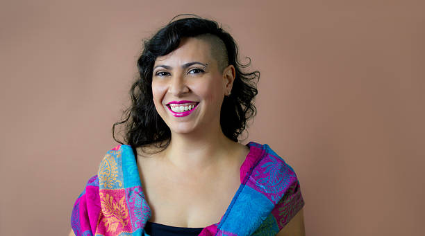istock Smiling woman with shaved-side hairstyle and colorful shawl on solid background. 2209006339