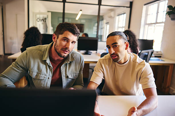 istock Two businessmen sitting at desk looking at computer and discussing 2209007405