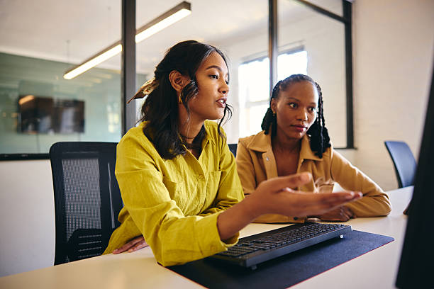 istock Two female business women sitting at desk using computer, one gesturing and explaining 2209007585
