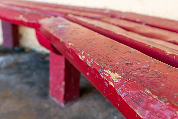 A worn red bench sits in a tranquil outdoor location, showing signs of age with its chipped paint and rustic charm, perfect for resting or pondering in nature.