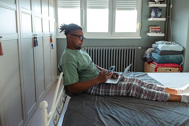 istock Man in casual wear using laptop while sitting on a bed at home 2209020959