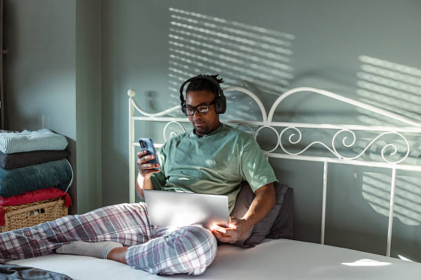 istock Man relaxing on bed using a laptop and smartphone with headphones on 2209021302