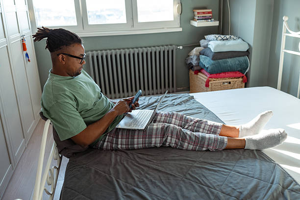 istock Man relaxing on bed using a laptop and smartphone in bedroom 2209021952