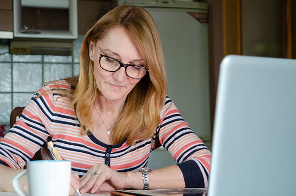 istock A dedicated senior woman sits at her table, carefully taking notes in her notebook as she follows an online course on her laptop 2209025163