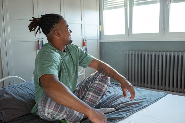istock Man sitting thoughtfully on bed near window during daytime 2209025410