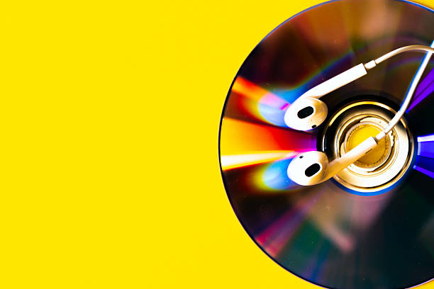 White earphones placed on a shiny compact disc with vibrant light reflections on a bright yellow background captured close up