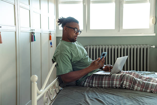 istock Man in casual wear using laptop while sitting on a bed at home 2209025914