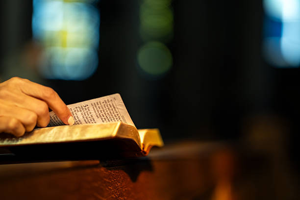 Close-up of hand on an open Bible, with warm lighting and blurred stained glass background in church.