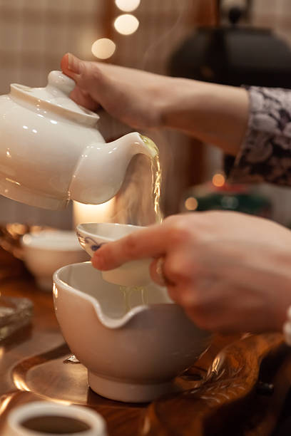 istock Pouring tea from white pot into cup in cozy setting with soft lighting. Ceremony 2209033407