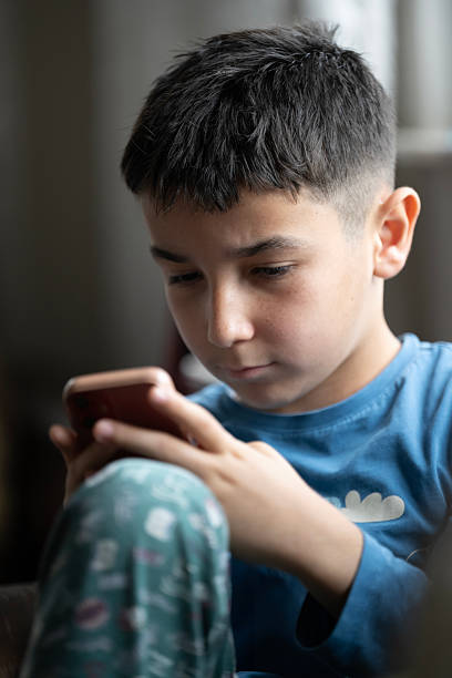 istock Preadolescent boy focused on watching content on smart phone at home 2209038497