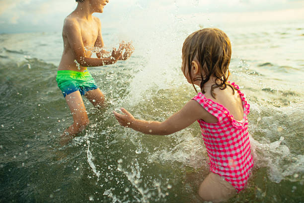 Brothers and sister are having fun on the beach. Kids are running, splashing and jumping into the sea and laughing.Sunny summer day evening.Nikon D850