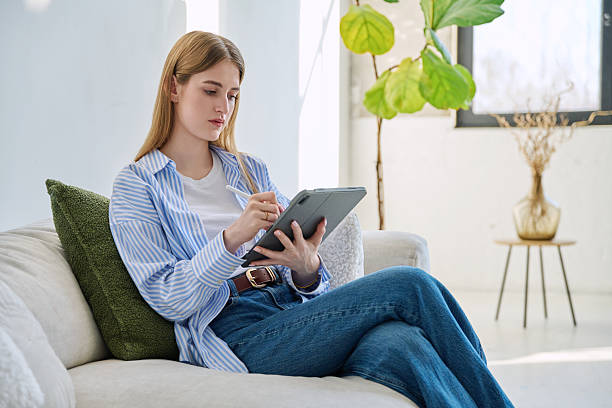 istock Young woman using digital tablet sitting on sofa at home 2209039601