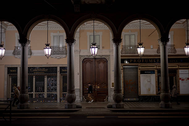 Turin, Italy - Nov 09 2021: Illuminated porticoes at night reveal closed shops and a few people walking along the covered walkway, with classic-style lanterns casting a warm light.