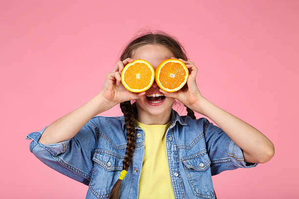 istock Young girl with orange fruit on pink background 2209041539