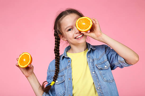 istock Young girl with orange fruit on pink background 2209043351
