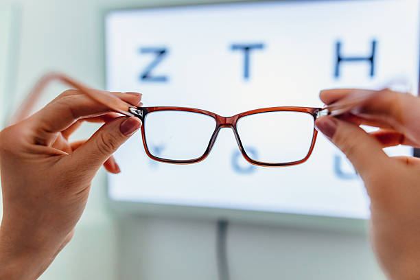 Hands Holding Eyeglasses With a Blurred Vision Test Chart in the Background