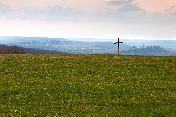 On a green field there is a Lonely Cross. Against the background of mountains and sky.
