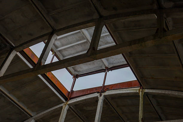 View from the inside of an abandoned concrete structure with broken openings in the roof through which the gray sky is visible.