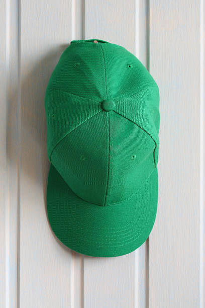 Close-up of a green baseball cap hanging on a white wooden wall, representing fashion, sport, or casual style
