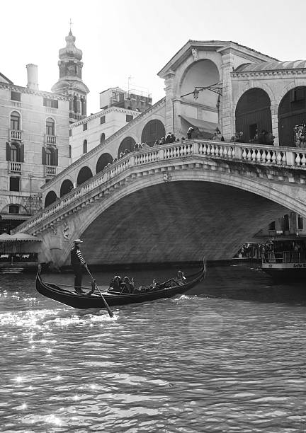03/02/2025 Venice. Italy\n\nGondolier sailing under Rialto Bridge in Venice with a couple of tourists - enjoying a romantic moment.