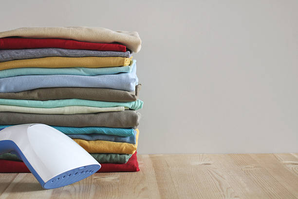 istock Steamer and stack of folded colorful t-shirts on wooden table 2209057924