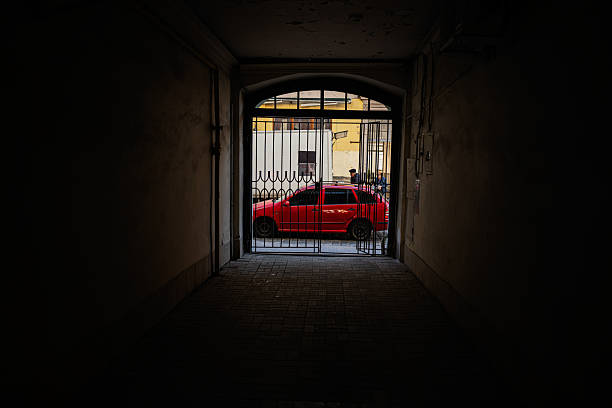 Lviv, Ukraine - April 06, 2025: A vibrant red car seen through a gate under an atmospheric dark passage.