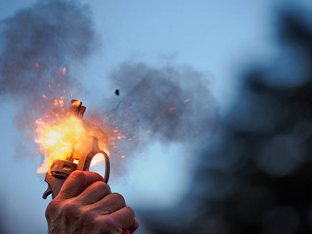 A rather close look at a starter pistol at a high school track meet. It has flames and smoke visible around the gun.