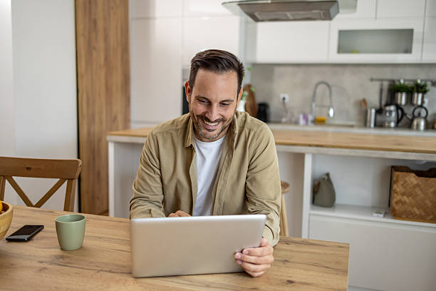 istock Smiling man working from home on laptop in kitchen 2209069615