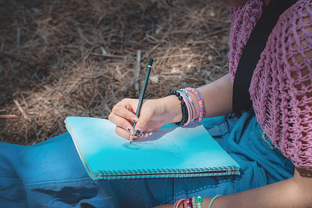 Young woman is drawing in her notebook she is sitting very concentrated drawing in pencil in her notebook.