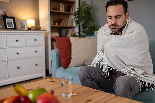 istock Sick man sitting on sofa wrapped in blanket, feeling cold 2209073266