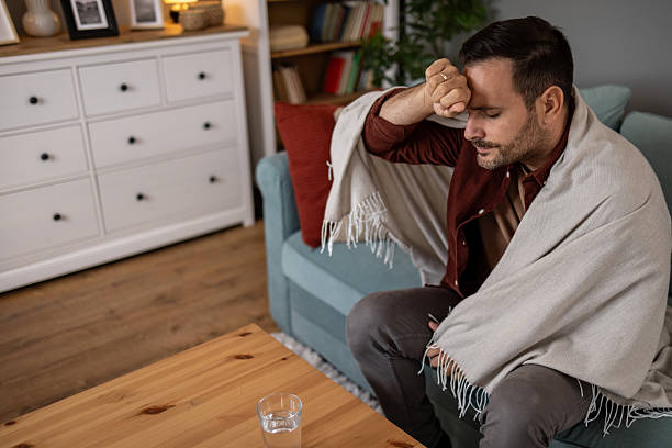 istock Sick man suffering from headache wrapped in blanket on sofa 2209073296