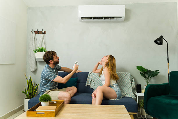 istock Couple relaxing on sofa using air conditioner remote control during summer heat 2209076996