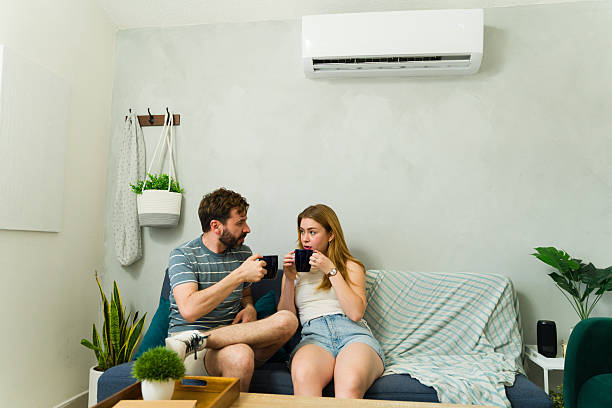 istock Relaxed couple sitting on sofa with air conditioning unit running 2209077173