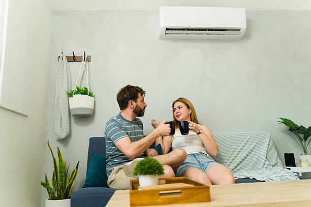 istock Couple relaxing on sofa under air conditioning, enjoying beverages 2209077178
