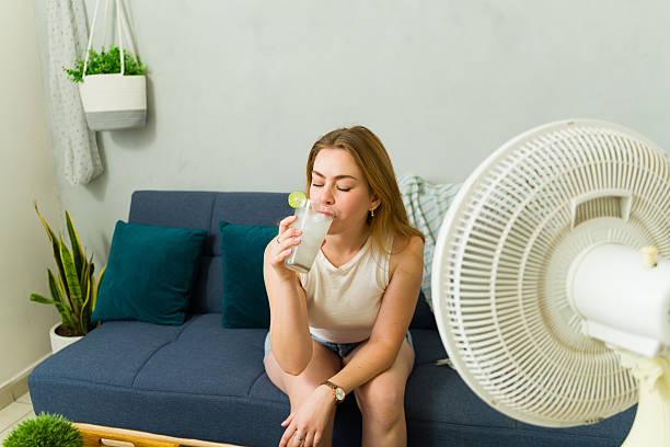 istock Woman drinking fresh lemonade and cooling down with fan during summer heat wave 2209077332