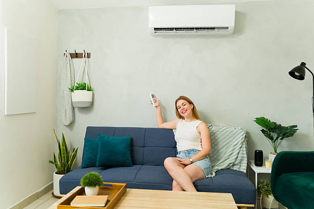 istock Beautiful woman relaxing on sofa using air conditioner remote control during summer heat 2209077376