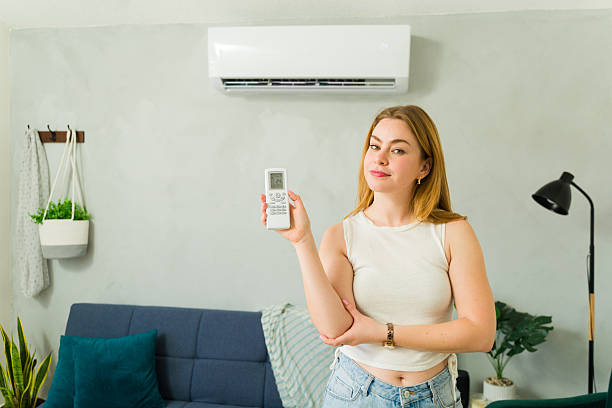 istock Woman holding remote control, using air conditioner at home during summer heat 2209077416
